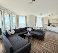 Wohnzimmer mit großer Couch, Esstisch und Boden mit Holzdekor.
