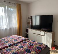 Schlafzimmer in einem Einfamilienhaus mit Fernseher, Blumenbettwäsche, gelbe Vorhänge, Fenster.
