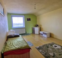 Einfaches Zimmer mit Bett, hellen Wänden und Boden in Holzoptik.
