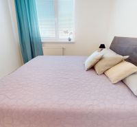 Helles Schlafzimmer in einer 3-Zimmer-Wohnung mit einer zarten lila Decke auf dem Bett.