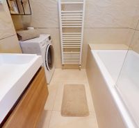 Badezimmer mit Badewanne, Waschmaschine, weißen Fliesen und Schrank in einer 3-Zimmer-Wohnung.