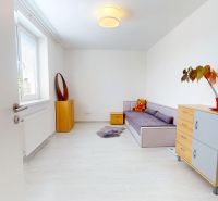 Ein Zimmer in einer 3-Zimmer-Wohnung mit einem Sofa, einer Kommode und einem Boden mit Holzdekor.