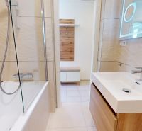 Badezimmer mit Badewanne und Waschbecken in einer 3-Zimmer-Wohnung, beige Fliesen, Holzdekor.