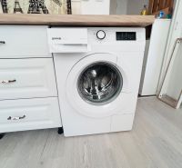Waschmaschine in der Küche eines Einzimmerapartments mit Holzboden und Holzarbeitsplatte.