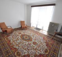 Wohnzimmer in einer Zweizimmerwohnung mit Teppich, zwei Sesseln und Fernseher.