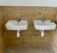 Zwei Waschbecken an der Wand mit Fliesen in Holzoptik in Lagern und Hallen.