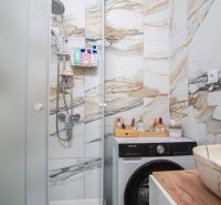 Badezimmer in einer 2-Zimmer-Wohnung mit Marmorfliesen, Duschkabine und Waschmaschine.