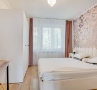 Helles Schlafzimmer mit Bett und zartem Blumendekor an der Tapete in einer 2-Zimmer-Wohnung.
