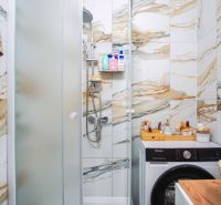 Badezimmer in einer 2-Zimmer-Wohnung mit Waschmaschine und Dusche, umgeben von Marmorbodenfliesen.