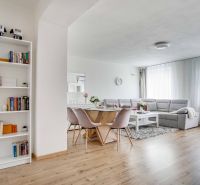 Wohnzimmer in einer Zweizimmerwohnung mit Holzboden, helle Sitzmöbel und Bücherregal.
