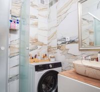Badezimmer einer Zweizimmerwohnung mit Waschmaschine, Waschbecken und Marmorverkleidung.