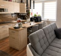 Wohnzimmer mit Küche, Holzboden, helle Schränke und graues Sofa.