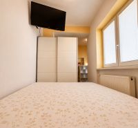 Schlafzimmer in einer Einzimmerwohnung mit Fernseher, Schrank und Fenster mit Rollläden.