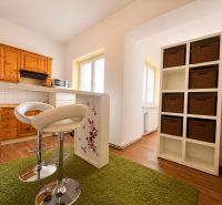 Küche in einer Einzimmerwohnung mit Schränken, Barhockern und einem Boden in Holzoptik.