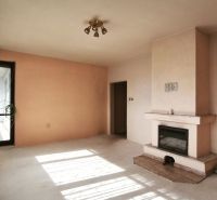 Innenraum eines Einfamilienhauses mit Kamin und großen Fenstern mit weißen Vorhängen.