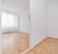 Weißes Zimmer mit großem Fenster und Holzboden in einer 3-Zimmer-Wohnung.