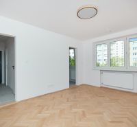 Eine Wohnung mit einem Holzboden, weißen Wänden und großen Fenstern.