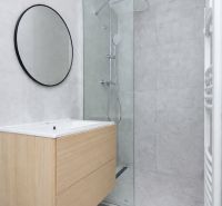 Badezimmer in einer 3-Zimmer-Wohnung mit moderner Duschkabine und Holzdekor auf dem Schrank.