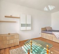 Ein Zimmer in einer Einzimmerwohnung mit einem Bett, einem Schrank und einem Boden in Holzoptik.