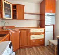 Küche in einer Einzimmerwohnung mit Holzboden und hellen Vorhängen.