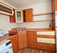 Küche mit Holzdekor in einer Einzimmerwohnung, ausgestattet mit Waschmaschine und Kühlschrank.