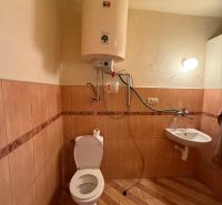 Badezimmer mit Toilette, Wassererhitzer, Waschbecken, Boden mit Holzdekor in einem Einfamilienhaus.