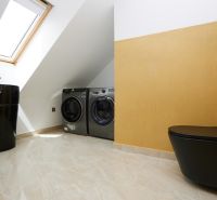 Badezimmer mit schwarzer Toilette, Waschbecken und Waschmaschinen in einer 3-Zimmer-Wohnung.