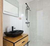 Badezimmer in einer 3-Zimmer-Wohnung mit schwarzem Waschbecken, Dusche und Holzelementen.