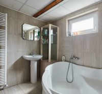 Badezimmer in der Hütte mit Badewanne, Waschbecken, Spiegel und Regalen für Toilettenartikel.