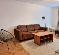 Wohnzimmer einer Zweizimmerwohnung mit braunem Sofa und Boden in Holzoptik.