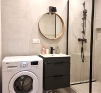 Badezimmer mit Waschmaschine, Duschkabine und rundem Spiegel in einer 2-Zimmer-Wohnung.