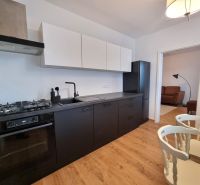 Küche in einer 2-Zimmer-Wohnung mit schwarzen Geräten und einem Boden in Holzoptik.