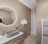 Badezimmer in einer 4-Zimmer-Wohnung mit rundem Spiegel und Waschbecken an beigefarbenen Wänden.