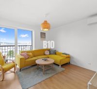 Wohnzimmer einer Vierzimmerwohnung mit gelbem Sofa und großem Fenster, Boden mit Holzdekor.
