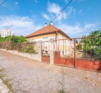 Ein Einfamilienhaus in Nitra mit einem Zaun und einem Schrägdach, im Hintergrund ein Plattenbau.