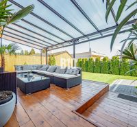 Ein Einfamilienhaus in Nitra mit überdachter Terrasse, Gartenmöbeln und einem Boden in Holzoptik.