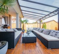 Die Terrasse des Einfamilienhauses in Nitra mit Rattanmöbeln und einem Boden in Holzoptik.