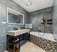 Badezimmer in einem Einfamilienhaus mit Badewanne, Steinverkleidung und großem Spiegel.