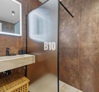 Badezimmer mit durchsichtiger Duschwand, steinernem Waschbecken und dekorativer Beleuchtung.