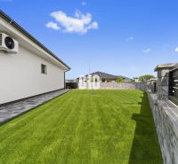 Der Garten eines Einfamilienhauses in Nitra mit Rasen und Steinpflaster an der Wand.