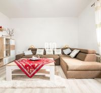 Wohnzimmer in einem Einfamilienhaus mit Ecksofa, Holzdekor und bunten Tischsets.