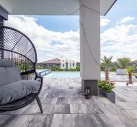 Ein Einfamilienhaus in Nitra mit Terrasse, Pool, Rattansessel und Palmen.