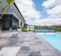 Ein Einfamilienhaus in Nitra mit Terrasse, Pool, Pflastersteinen und exotischen Pflanzen.