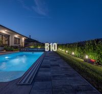 Nachtgarten bei einem Einfamilienhaus in Nitra mit beleuchtetem Pool und Terrasse.