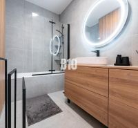 Badezimmer mit Holzdekor in einem Einfamilienhaus, mit Badewanne und ovalem Spiegel mit Beleuchtung.