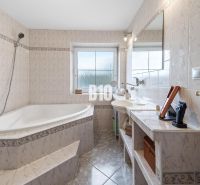 Ein Badezimmer im Einfamilienhaus mit einer Eckbadewanne und einem Fenster, helle Fliesen.