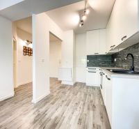 Küchenbereich in einer 2-Zimmer-Wohnung mit Holzboden und weißen Schränken.