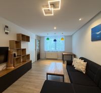 Wohnzimmer in einer 3-Zimmer-Wohnung mit Holzboden und schwarzem Sofa.