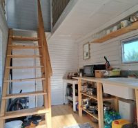 Innenraum einer Hütte mit Treppe, Küche und Boden in Holzoptik.