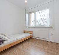 Einzelbett und Fenster mit weißen Vorhängen in einer 3-Zimmer-Wohnung auf einem Boden mit Holzdekor.